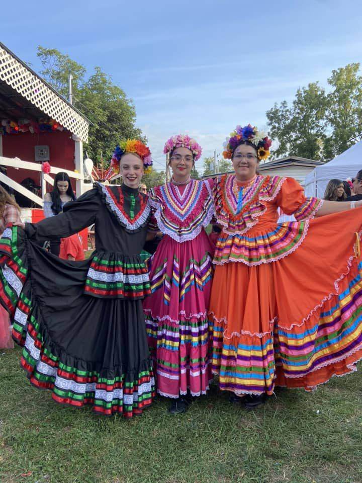 Three dancers in colorful dresses and flower crowns