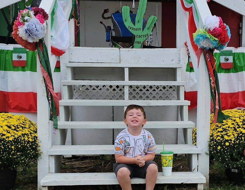 A child sitting on the stage steps next to the Crooked Cactus Band sign
