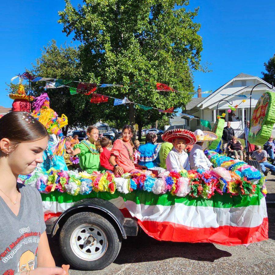 Children in traditional dress and sombreros on a papel picado-decorated float
